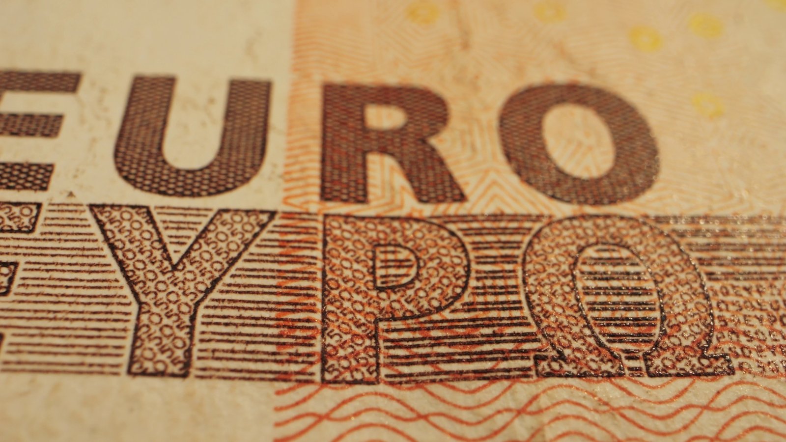 Extreme close-up of a euro banknote showing the word EURO in Latin and Greek letters on orange and cream paper