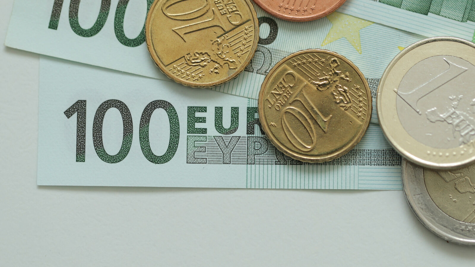 Euro coins lying on 100-euro banknotes on a pale table