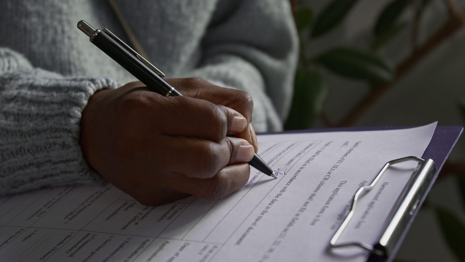 Close-up of a hand filling in a printed application form on a clipboard with a pen