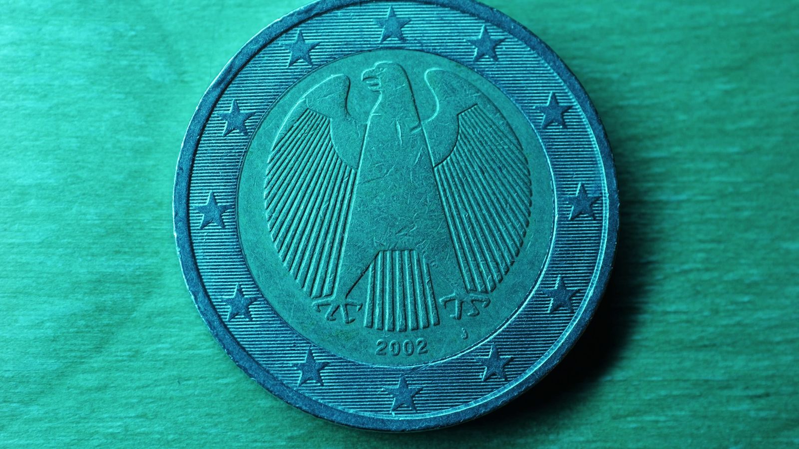 Close-up of a German two-euro coin showing the federal eagle, on a green surface