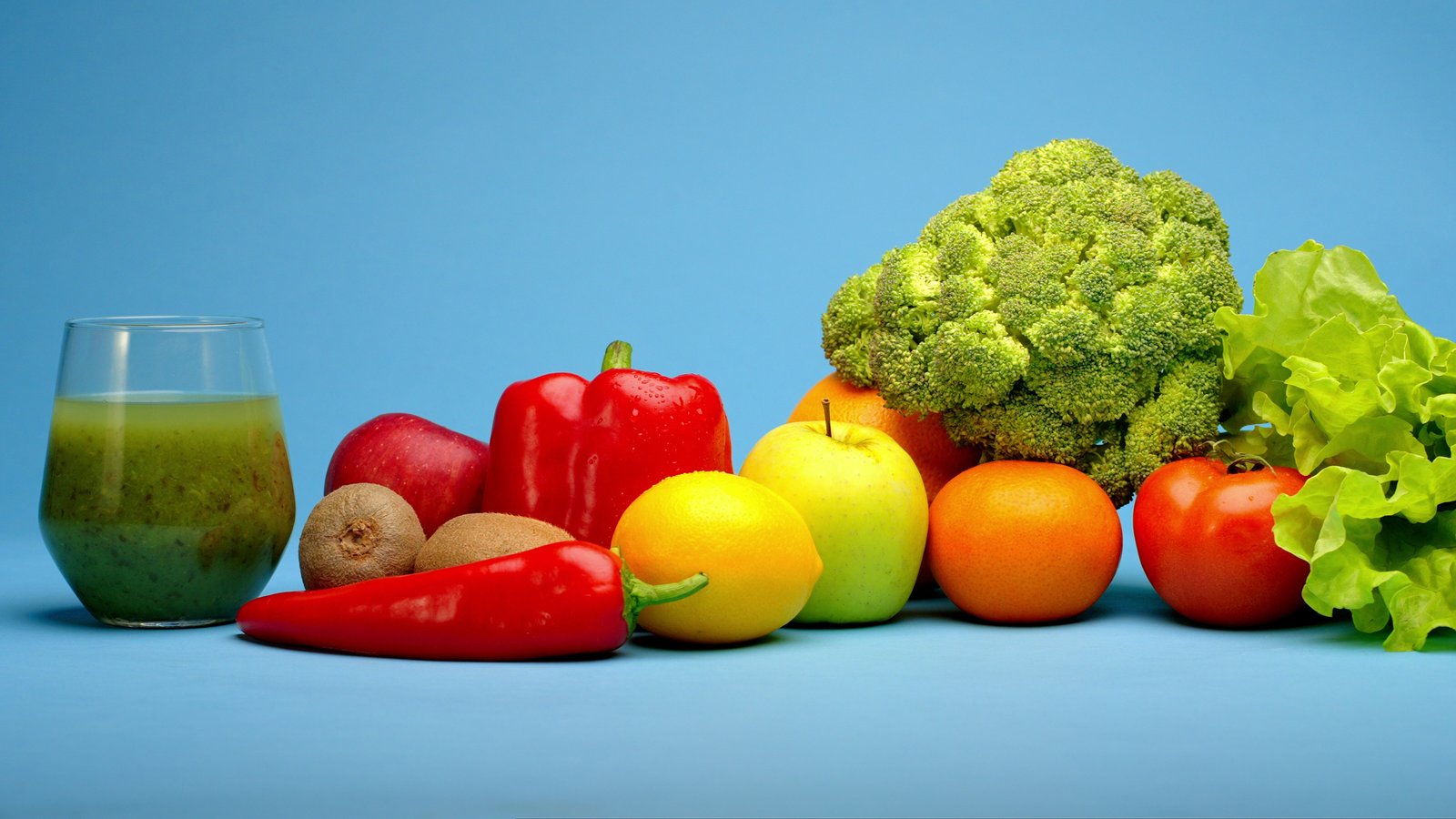 Fresh fruit and vegetables and a glass of green juice on a blue table